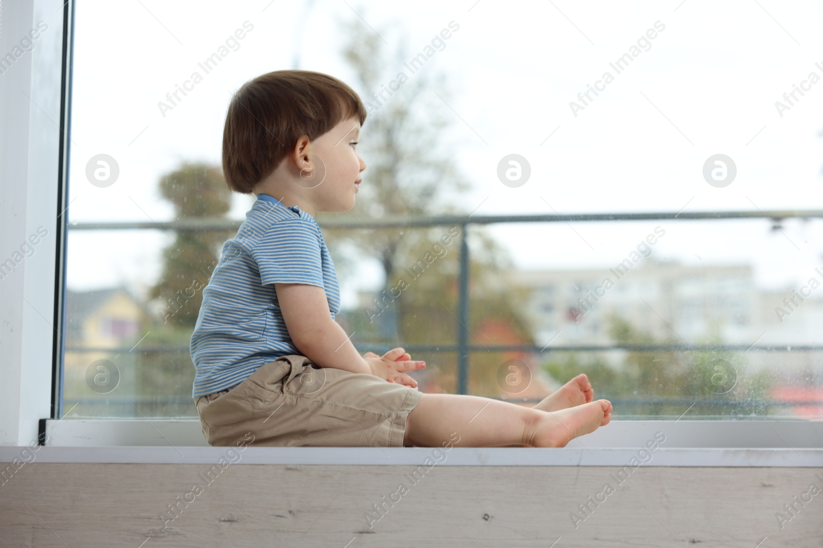 Photo of Little boy sitting on window sill. Child in danger