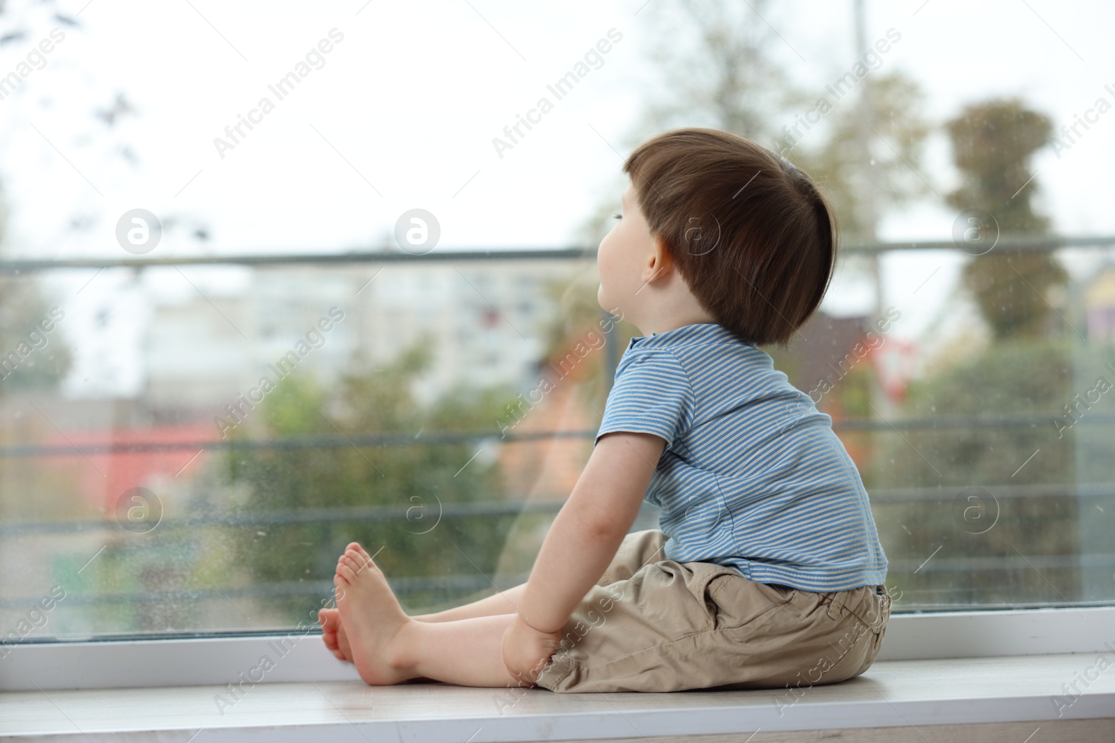 Photo of Little boy sitting on window sill. Child in danger