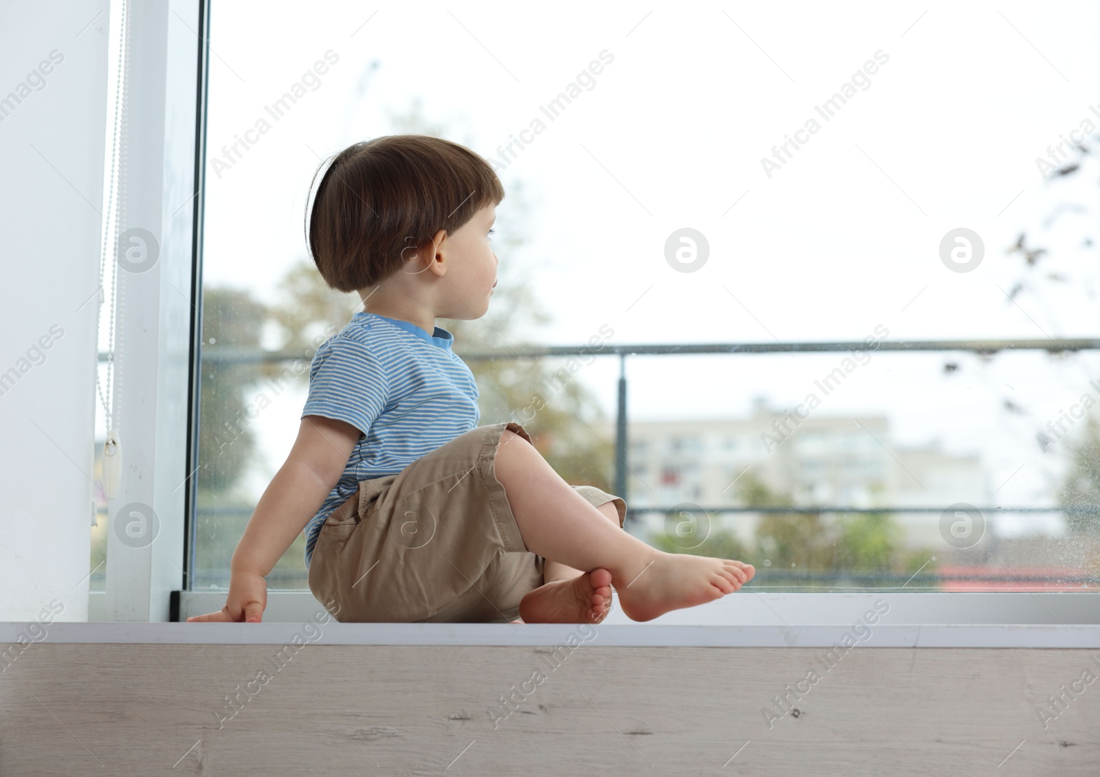 Photo of Little boy sitting on window sill, space for text. Child in danger