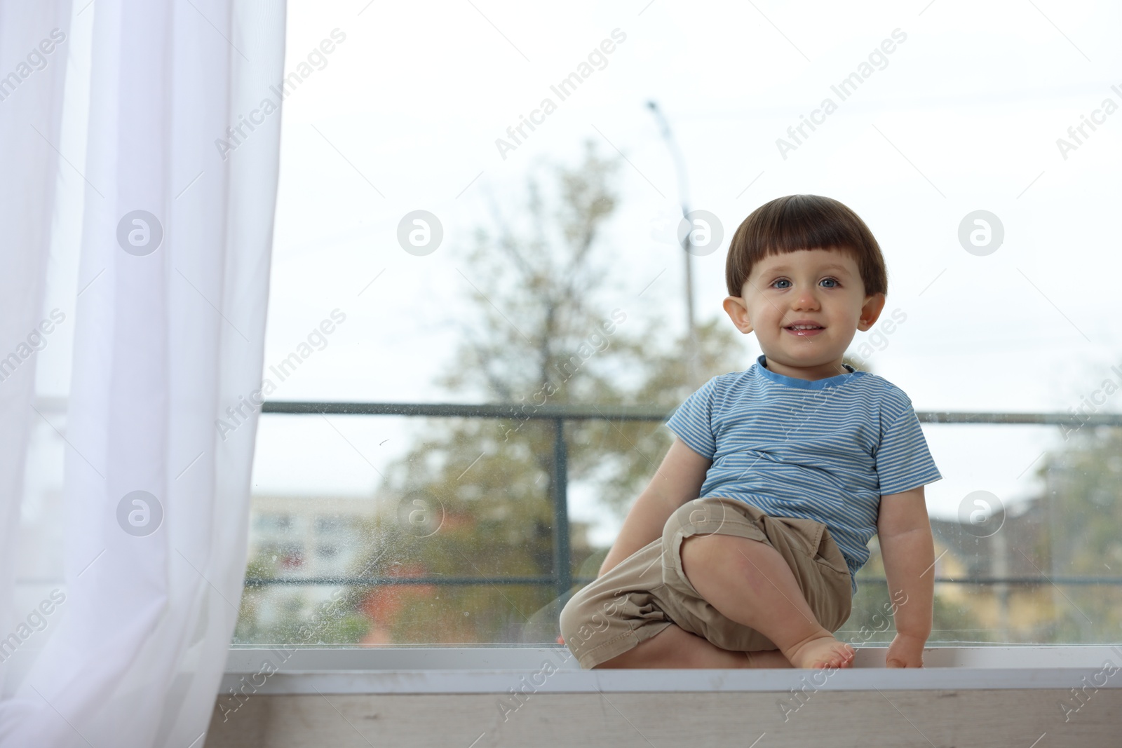 Photo of Little boy sitting on window sill, space for text. Child in danger