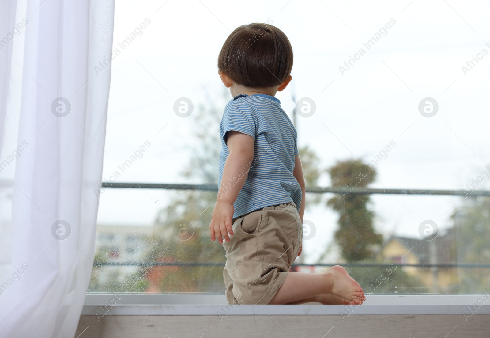 Photo of Little boy on window sill. Child in danger