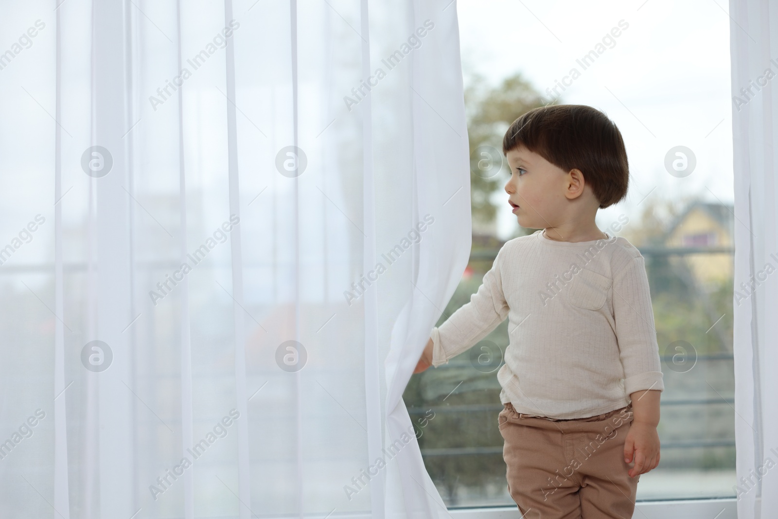 Photo of Little boy near window at home, space for text. Child in danger