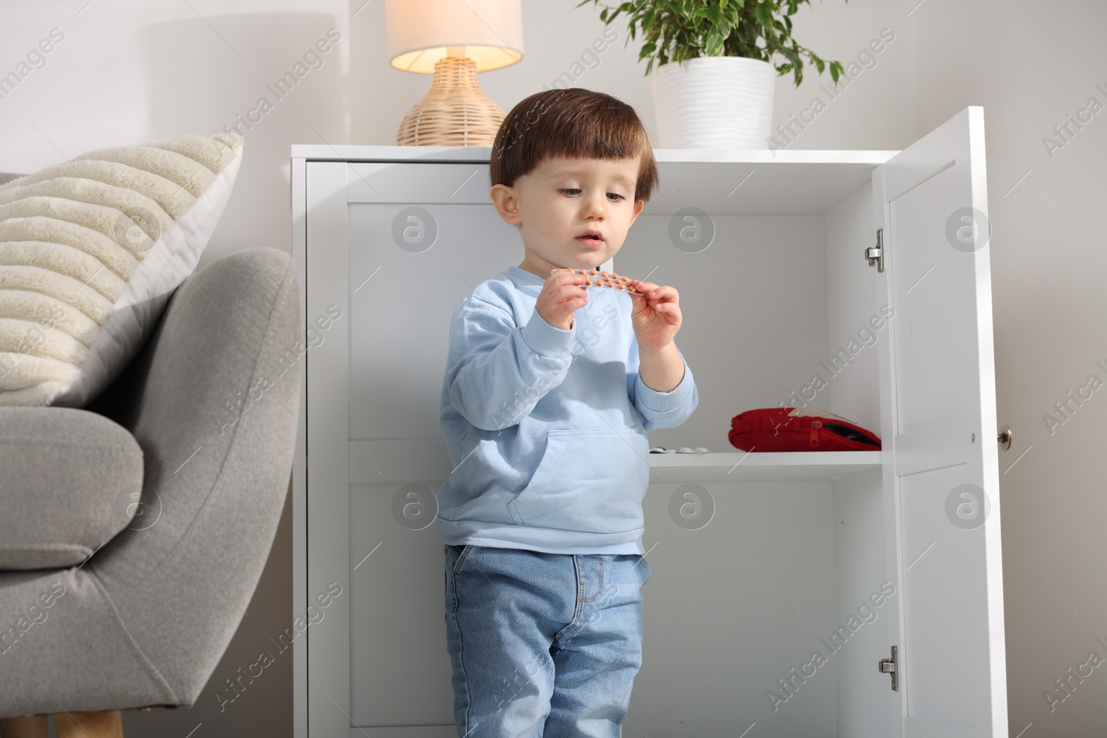 Photo of Little boy with pills near cabinet at home. Child in danger