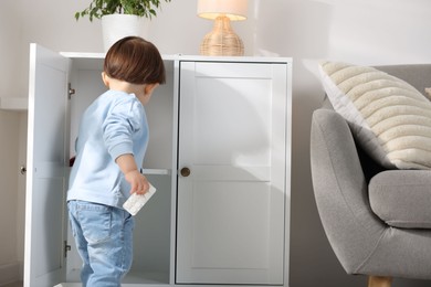 Photo of Little boy finding cabinet with pills at home, back view. Child in danger