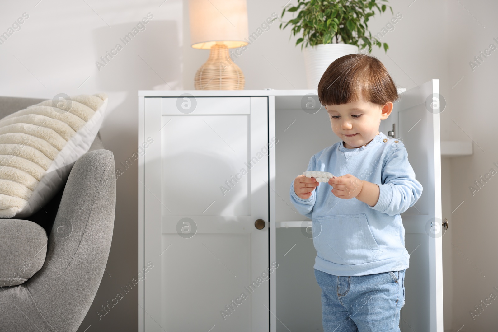 Photo of Little boy with pills near cabinet at home. Child in danger