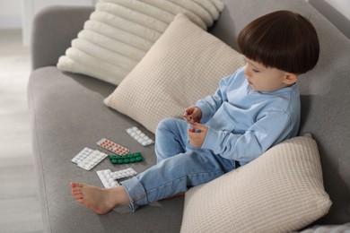 Photo of Little boy playing with pills on sofa at home. Child in danger