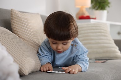 Photo of Little boy playing with pills on sofa at home. Child in danger