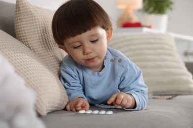 Photo of Little boy playing with pills on sofa at home. Child in danger