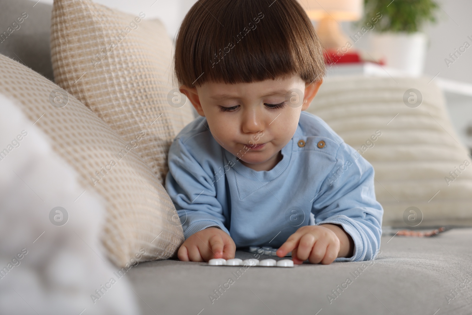 Photo of Little boy playing with pills on sofa at home. Child in danger