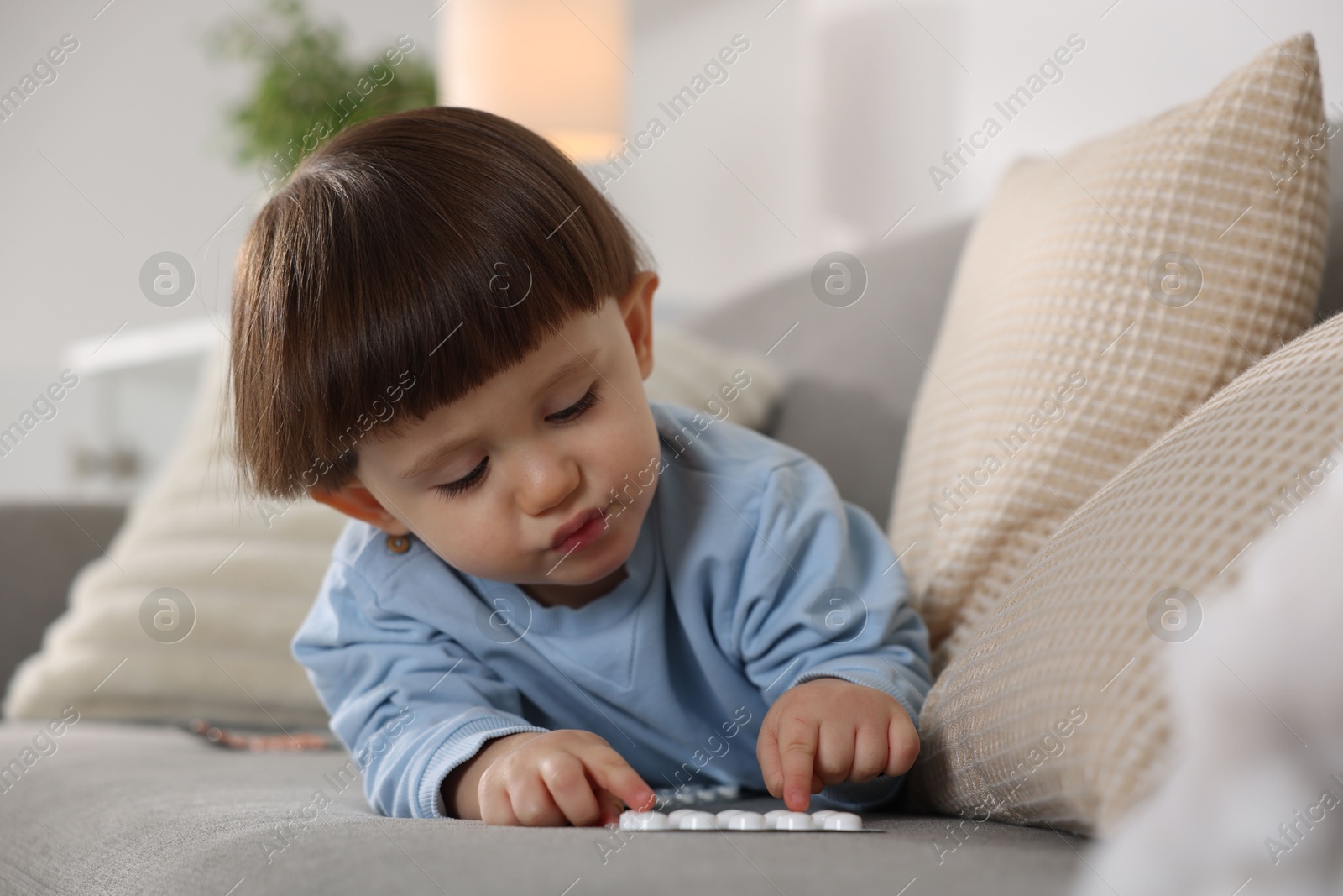 Photo of Little boy playing with pills on sofa at home. Child in danger