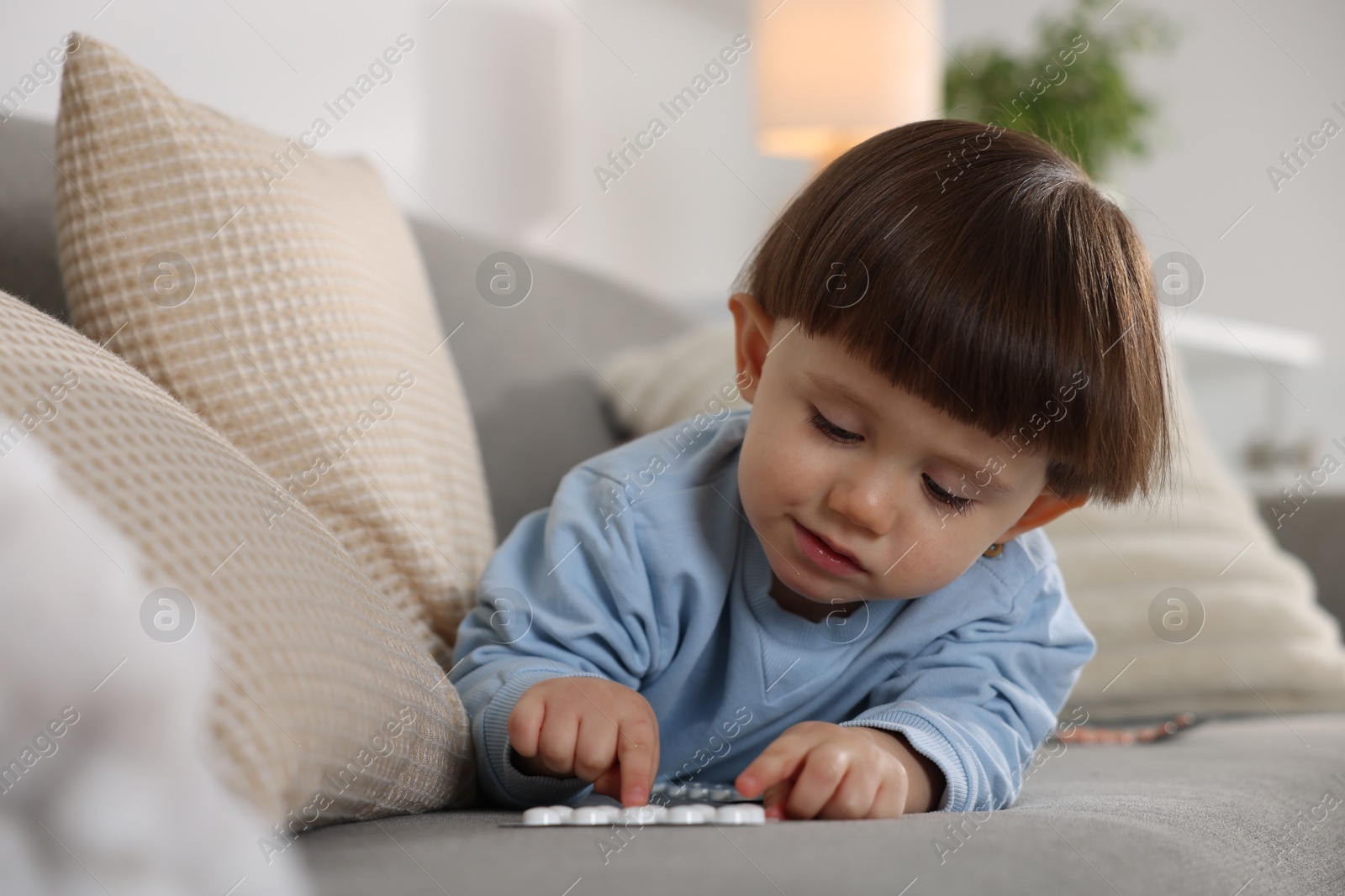 Photo of Little boy playing with pills on sofa at home. Child in danger