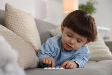 Photo of Little boy playing with pills on sofa at home. Child in danger