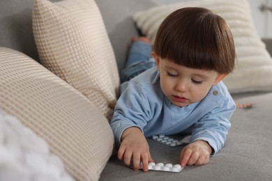 Little boy playing with pills on sofa at home. Child in danger