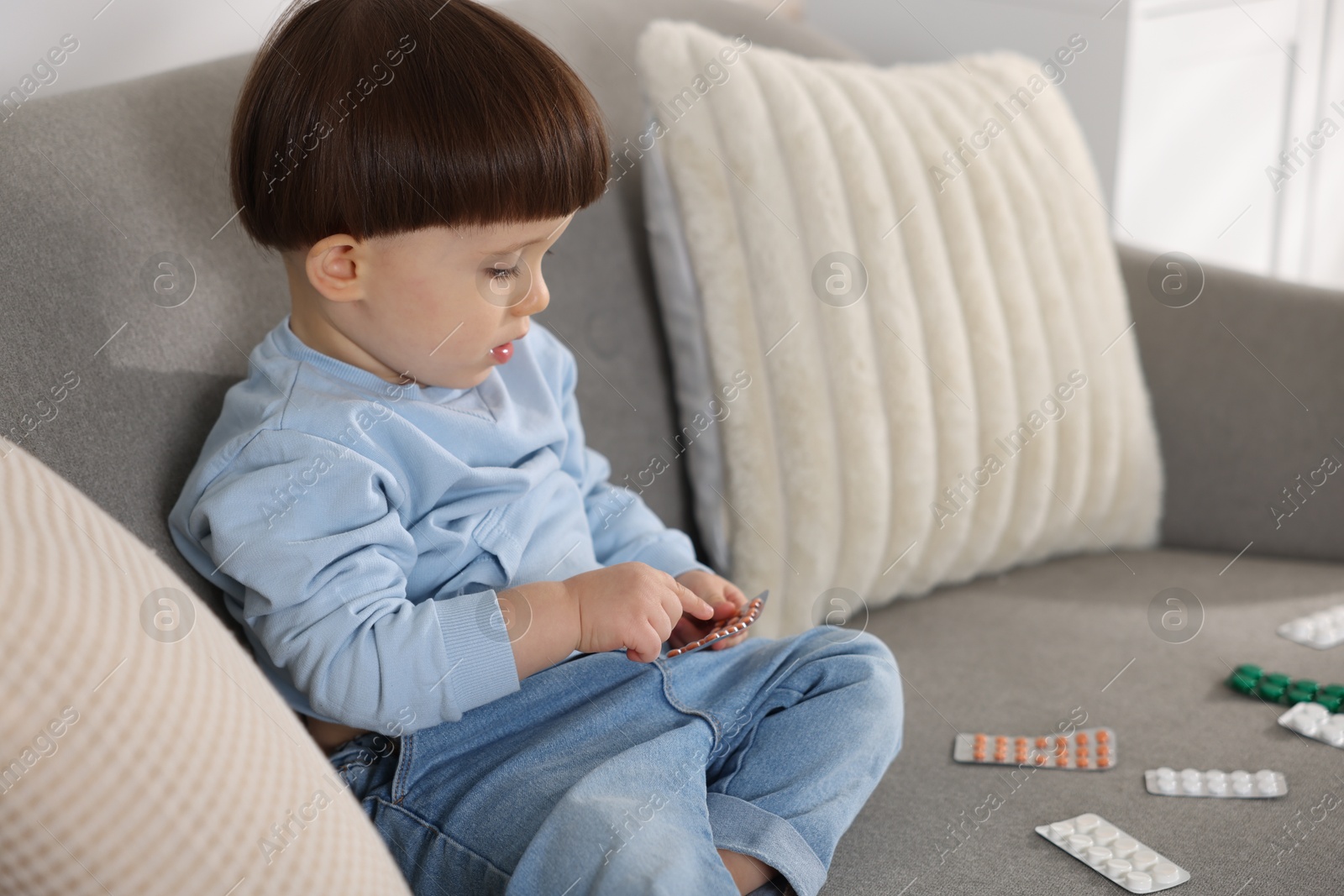 Photo of Little boy playing with pills on sofa at home. Child in danger