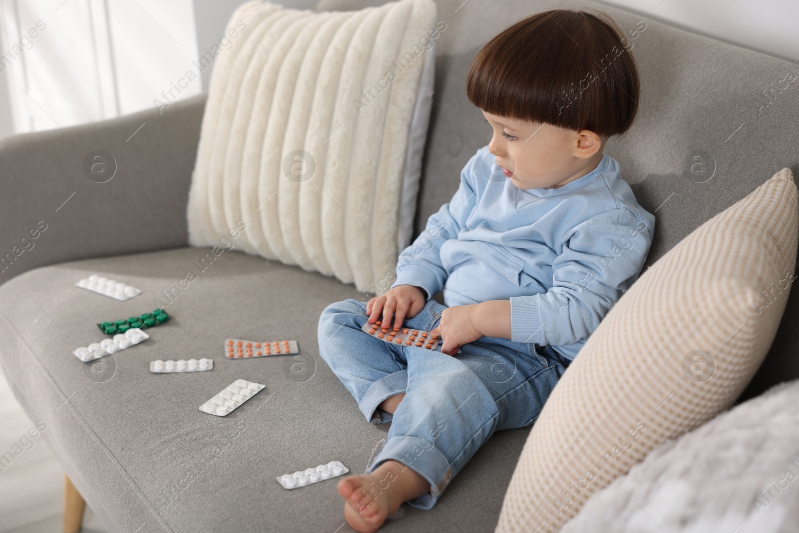 Photo of Little boy playing with pills on sofa at home. Child in danger