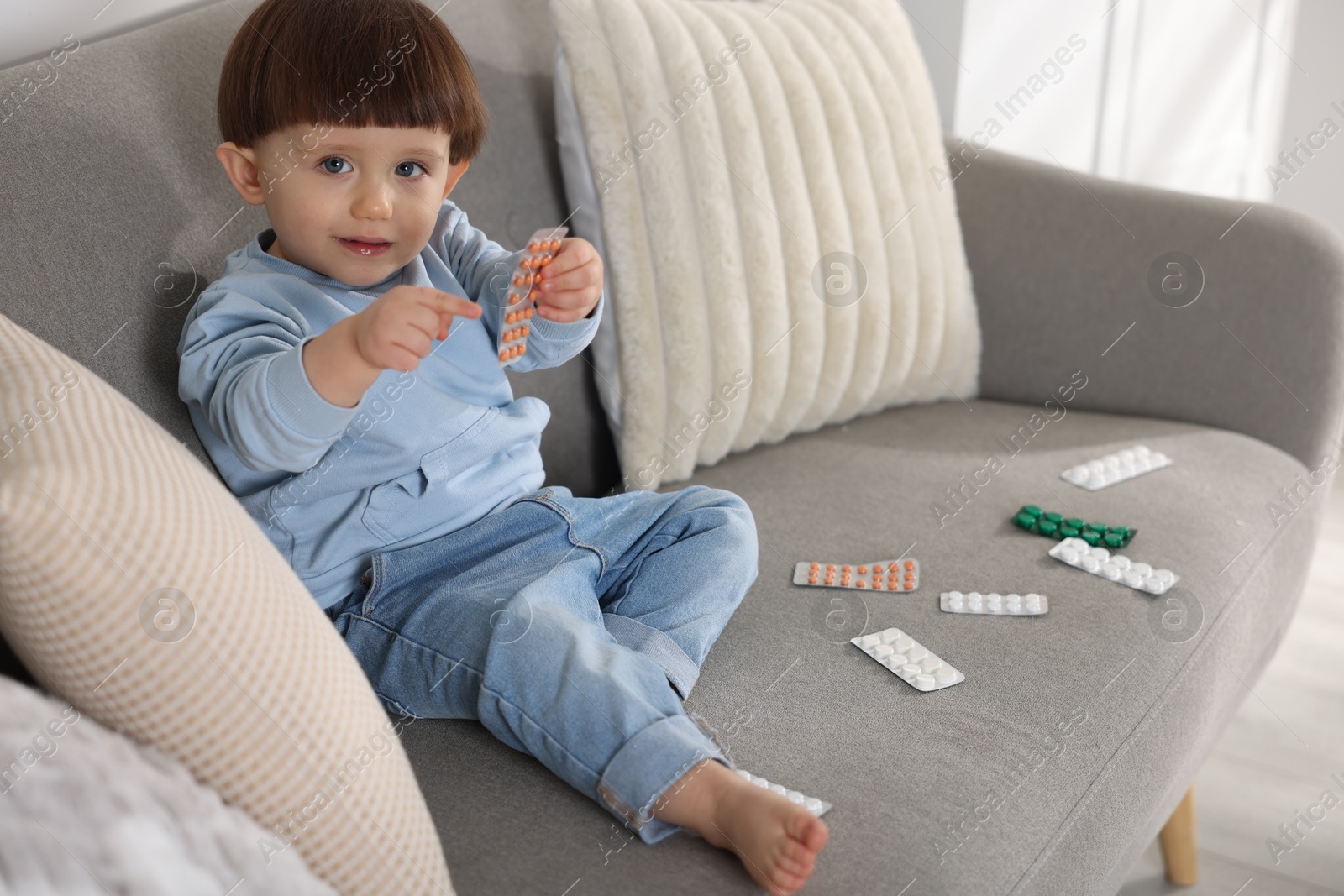 Photo of Little boy playing with pills on sofa at home. Child in danger