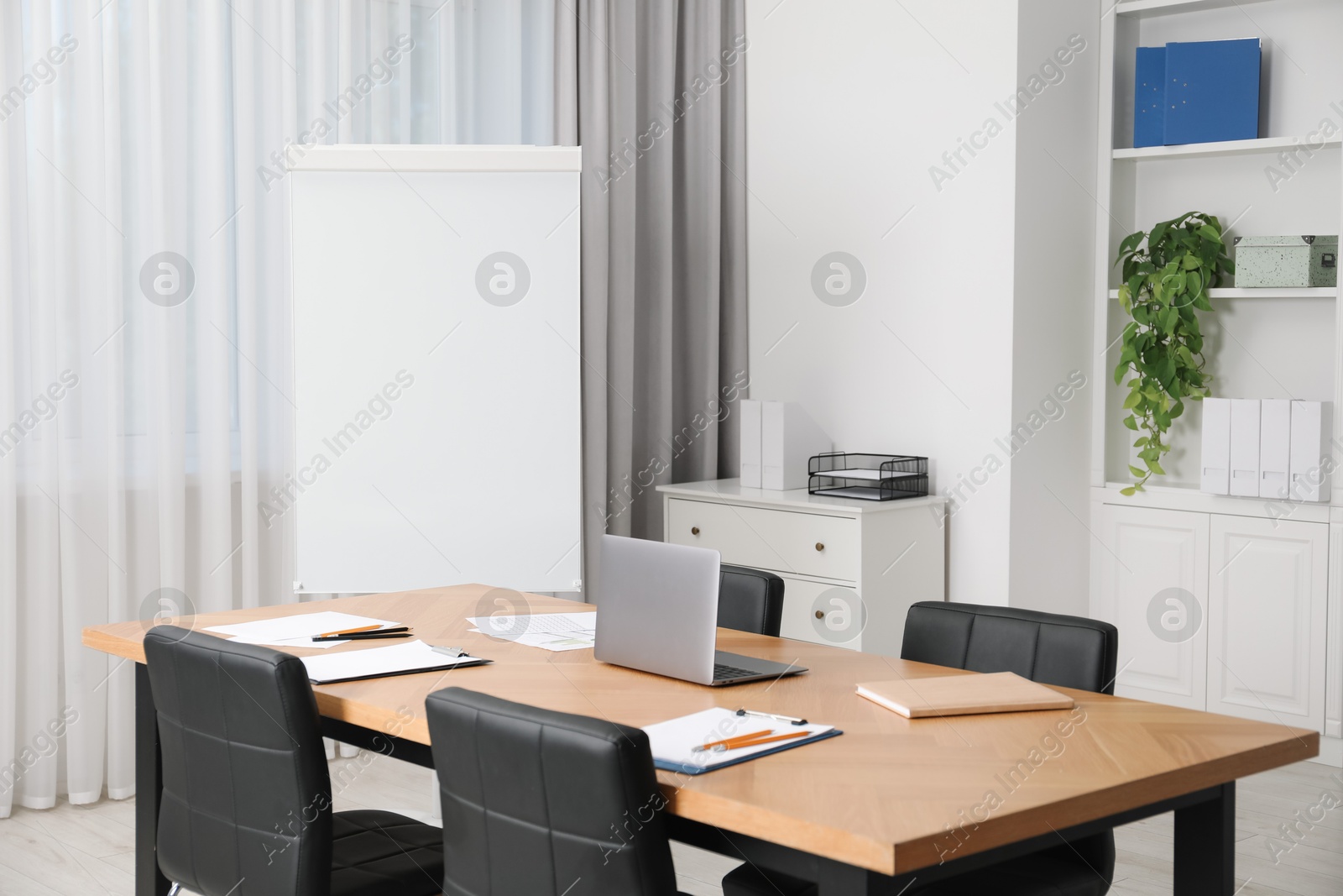 Photo of Flip chart, wooden table and chairs in conference room. Mockup for design