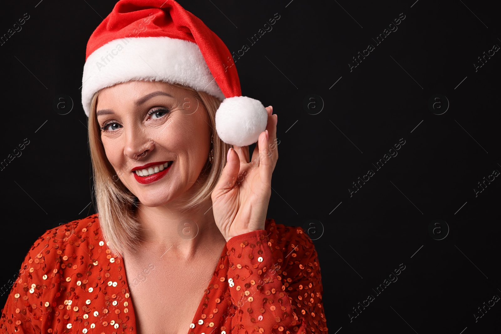 Photo of Smiling woman with perfect makeup in Santa hat celebrating Christmas on black background. Space for text