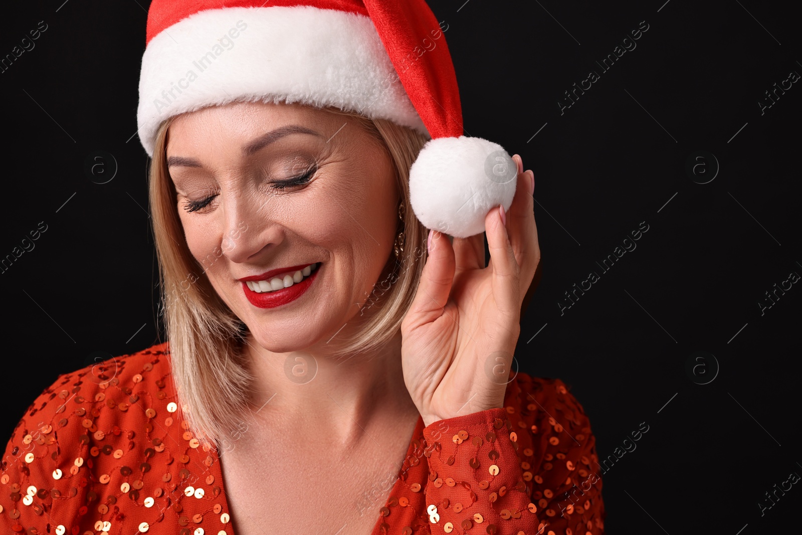 Photo of Smiling woman with perfect makeup in Santa hat celebrating Christmas on black background