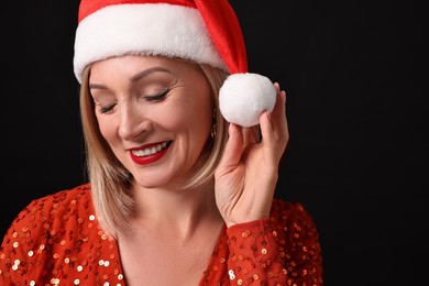 Photo of Smiling woman with perfect makeup in Santa hat celebrating Christmas on black background