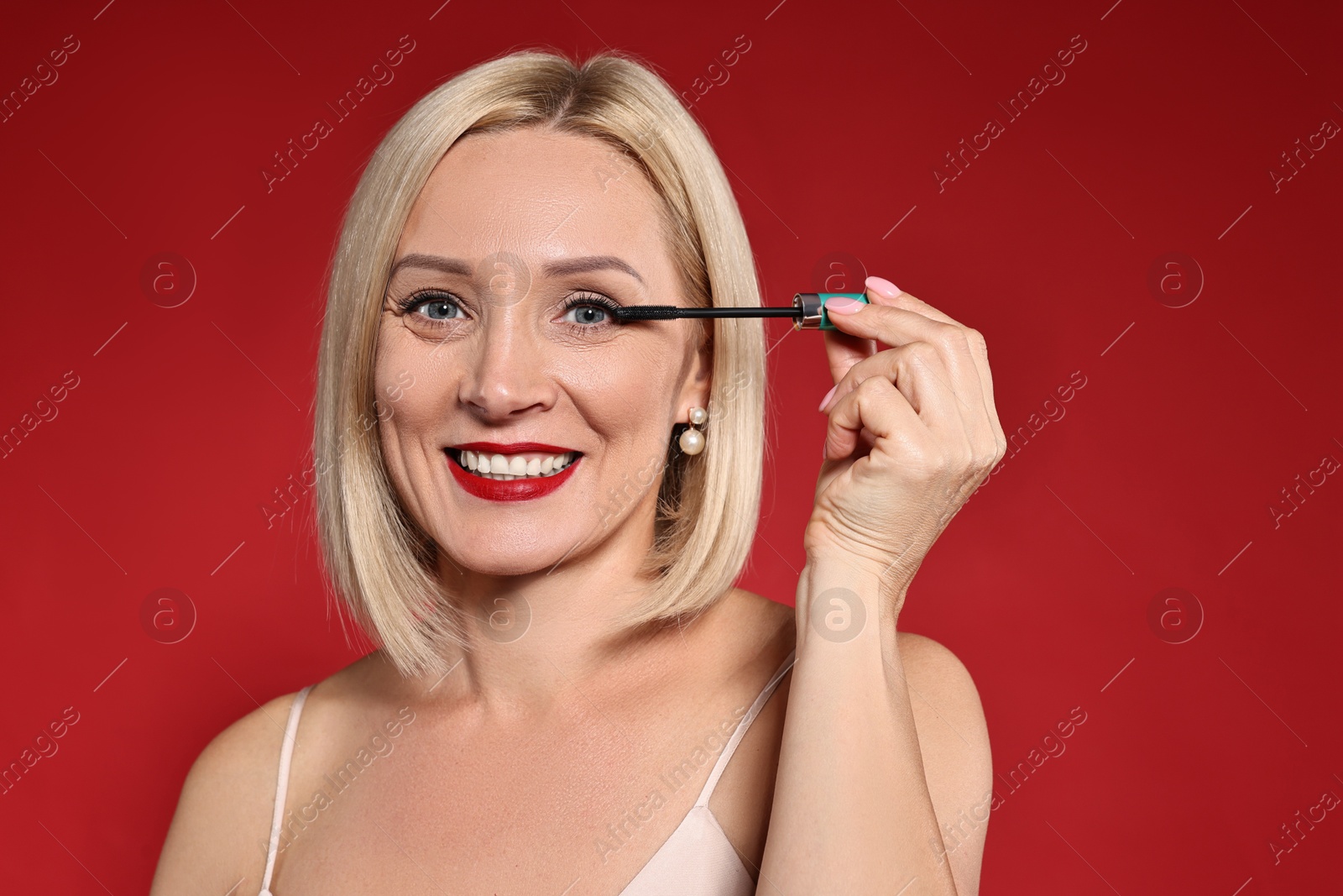 Photo of Smiling woman with makeup brush on red background