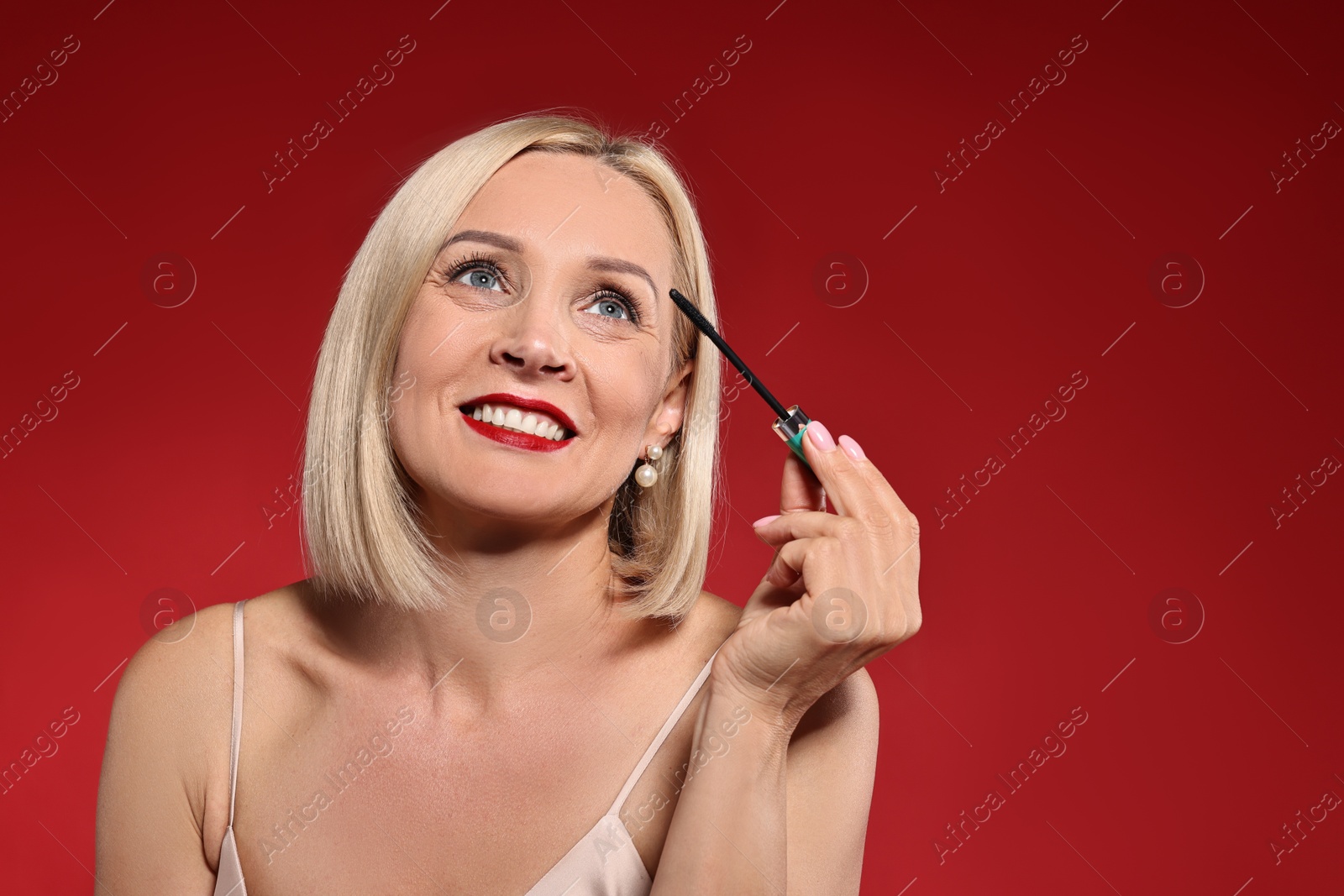 Photo of Smiling woman with makeup brush on red background. Space for text