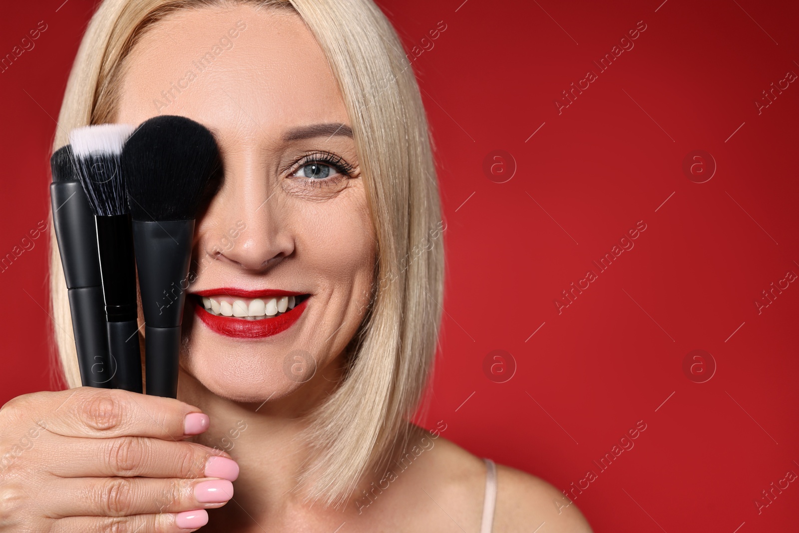 Photo of Smiling woman with different makeup brushes on red background. Space for text