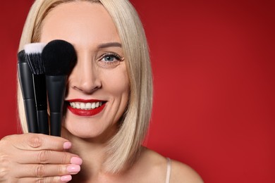 Photo of Smiling woman with different makeup brushes on red background. Space for text