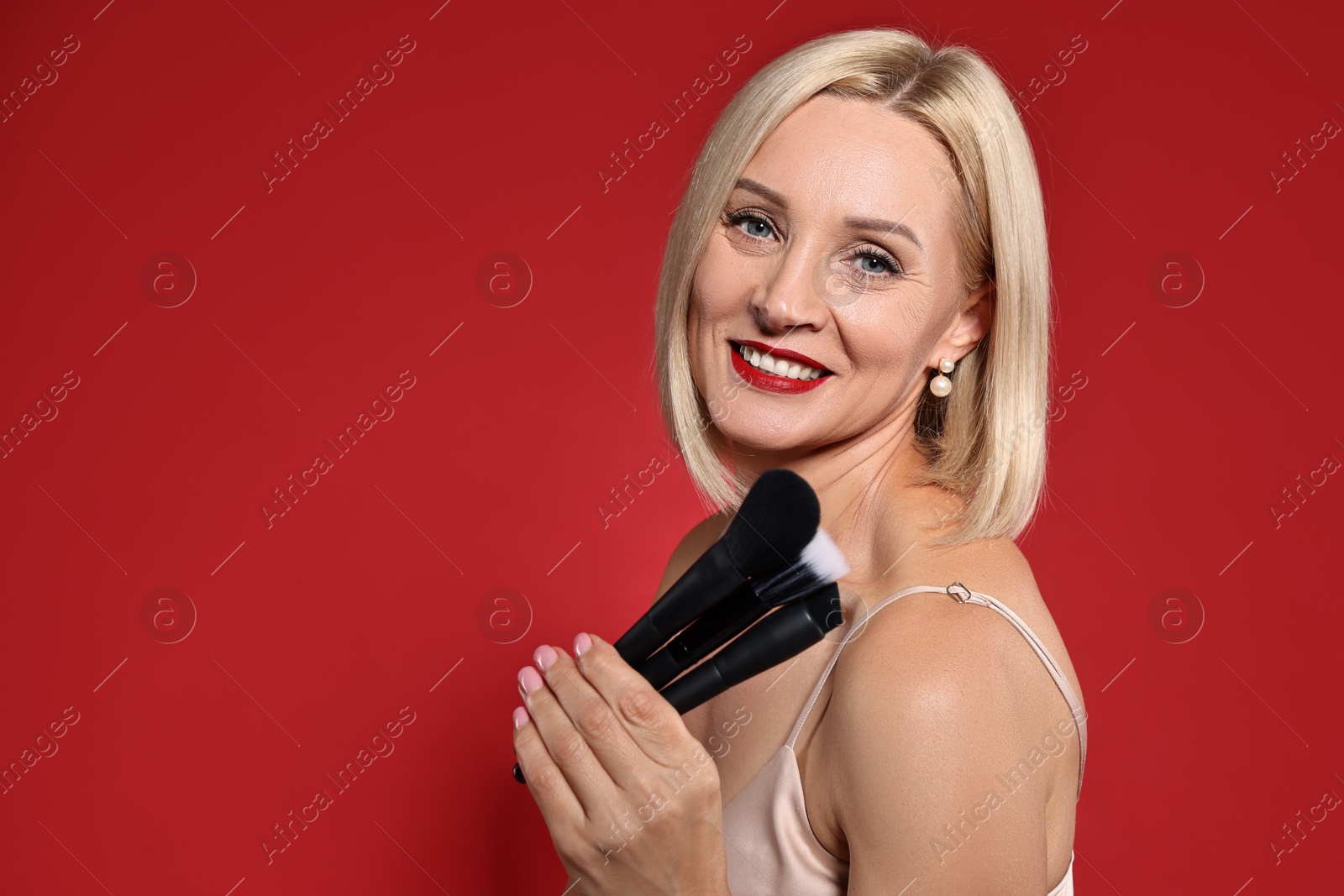 Photo of Smiling woman with different makeup brushes on red background. Space for text