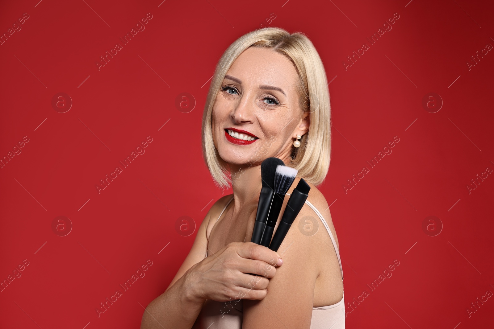 Photo of Smiling woman with different makeup brushes on red background