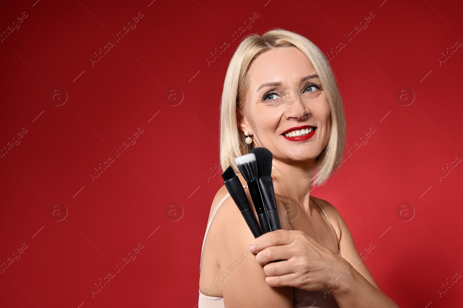 Photo of Smiling woman with different makeup brushes on red background. Space for text