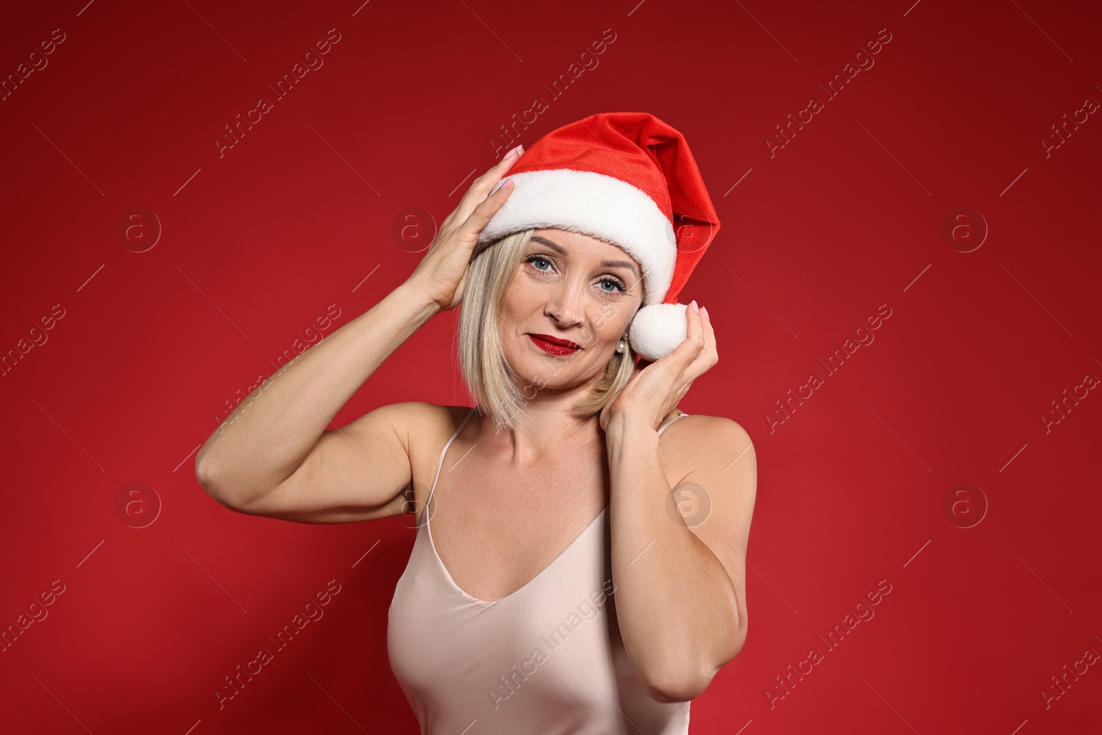 Photo of Woman with perfect makeup in Santa hat celebrating Christmas on red background