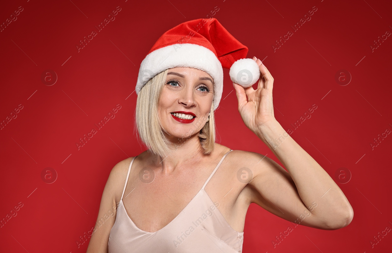 Photo of Smiling woman with perfect makeup in Santa hat celebrating Christmas on red background