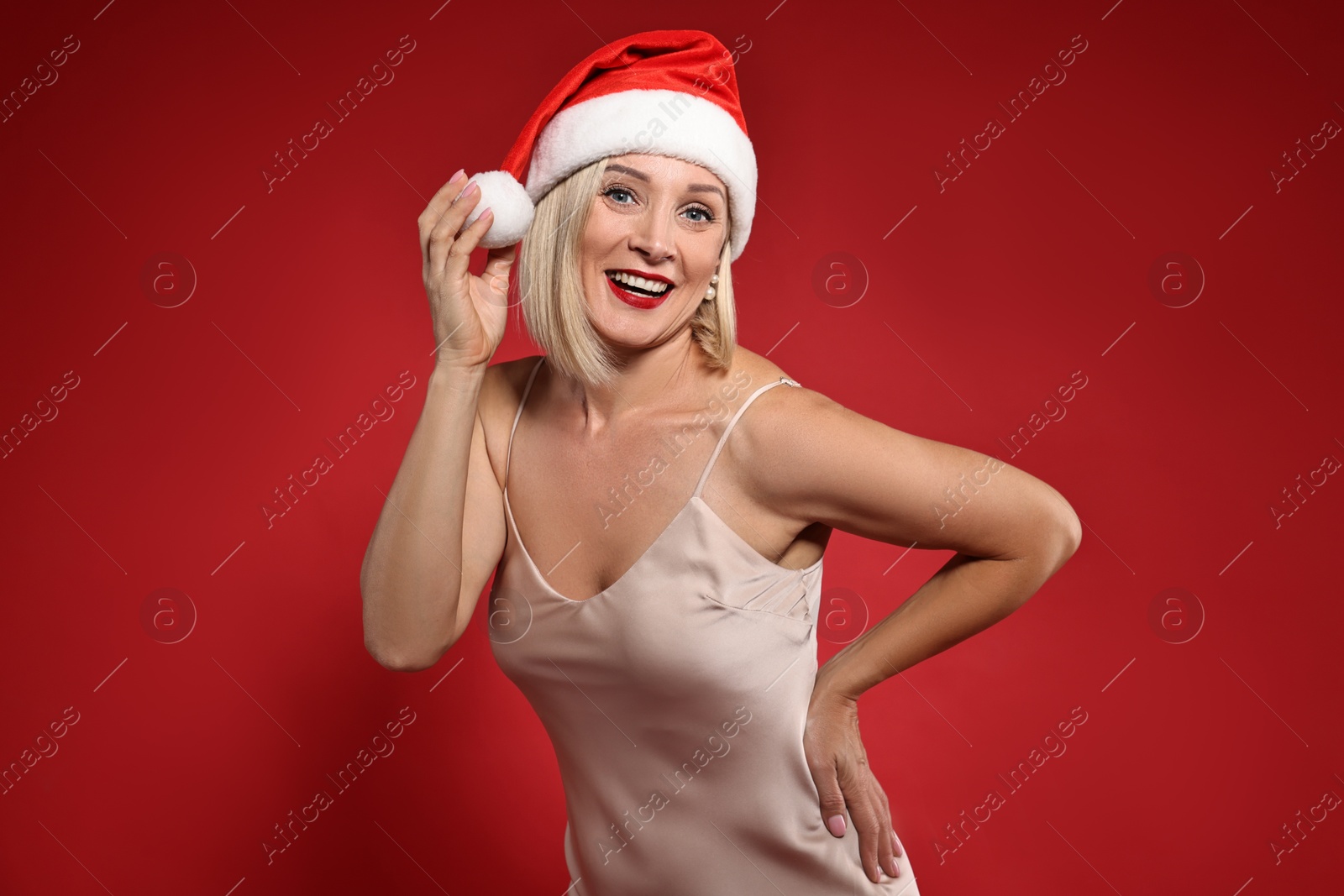 Photo of Smiling woman with perfect makeup in Santa hat celebrating Christmas on red background