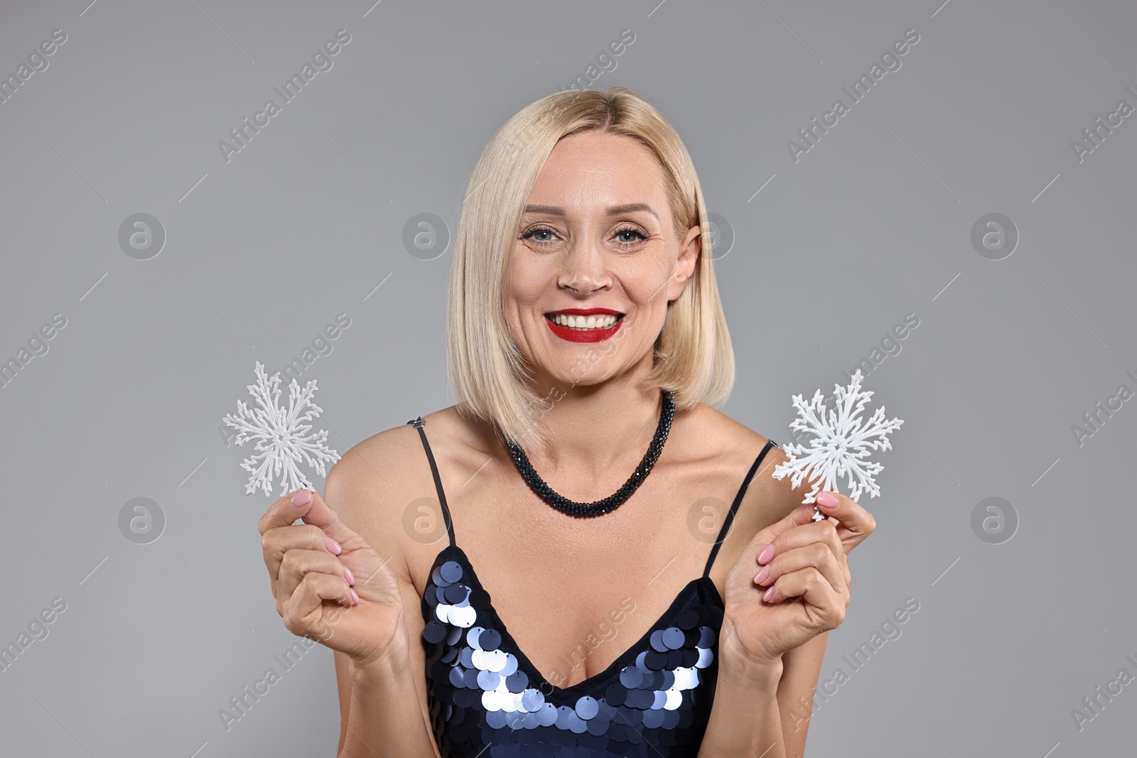 Photo of Smiling woman with decorative snowflakes on grey background. Christmas celebration