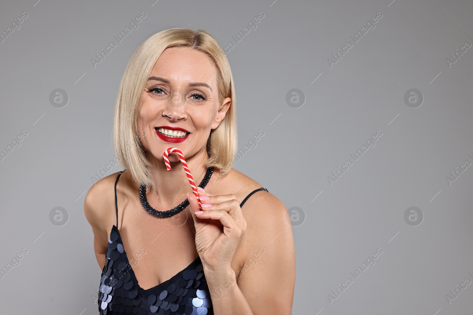 Photo of Smiling woman with Christmas candy cane on grey background. Space for text