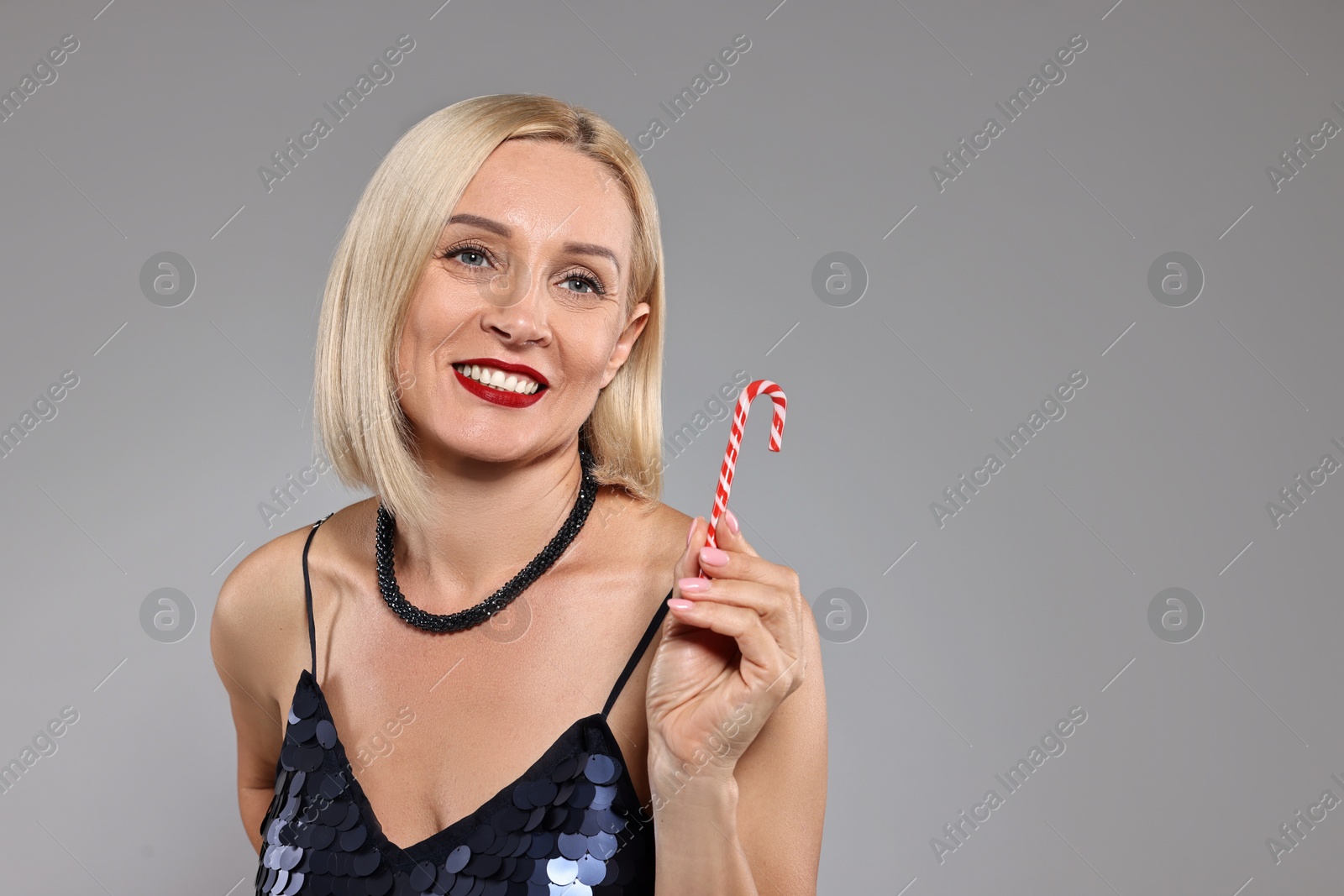 Photo of Smiling woman with Christmas candy cane on grey background. Space for text