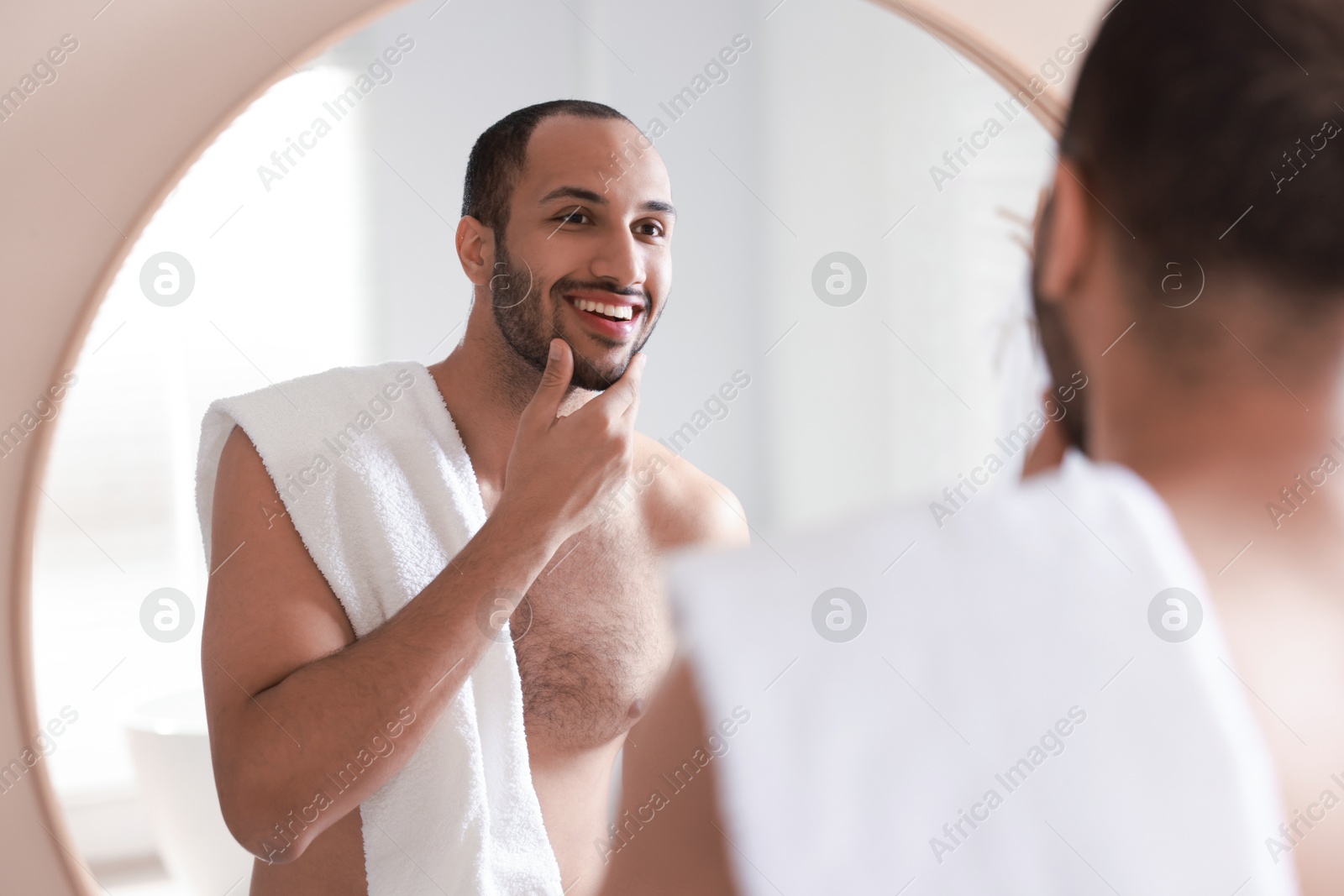 Photo of Smiling man with towel looking at mirror in bathroom