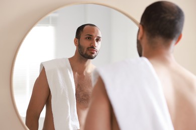 Photo of Handsome man with towel looking at mirror in bathroom, back view