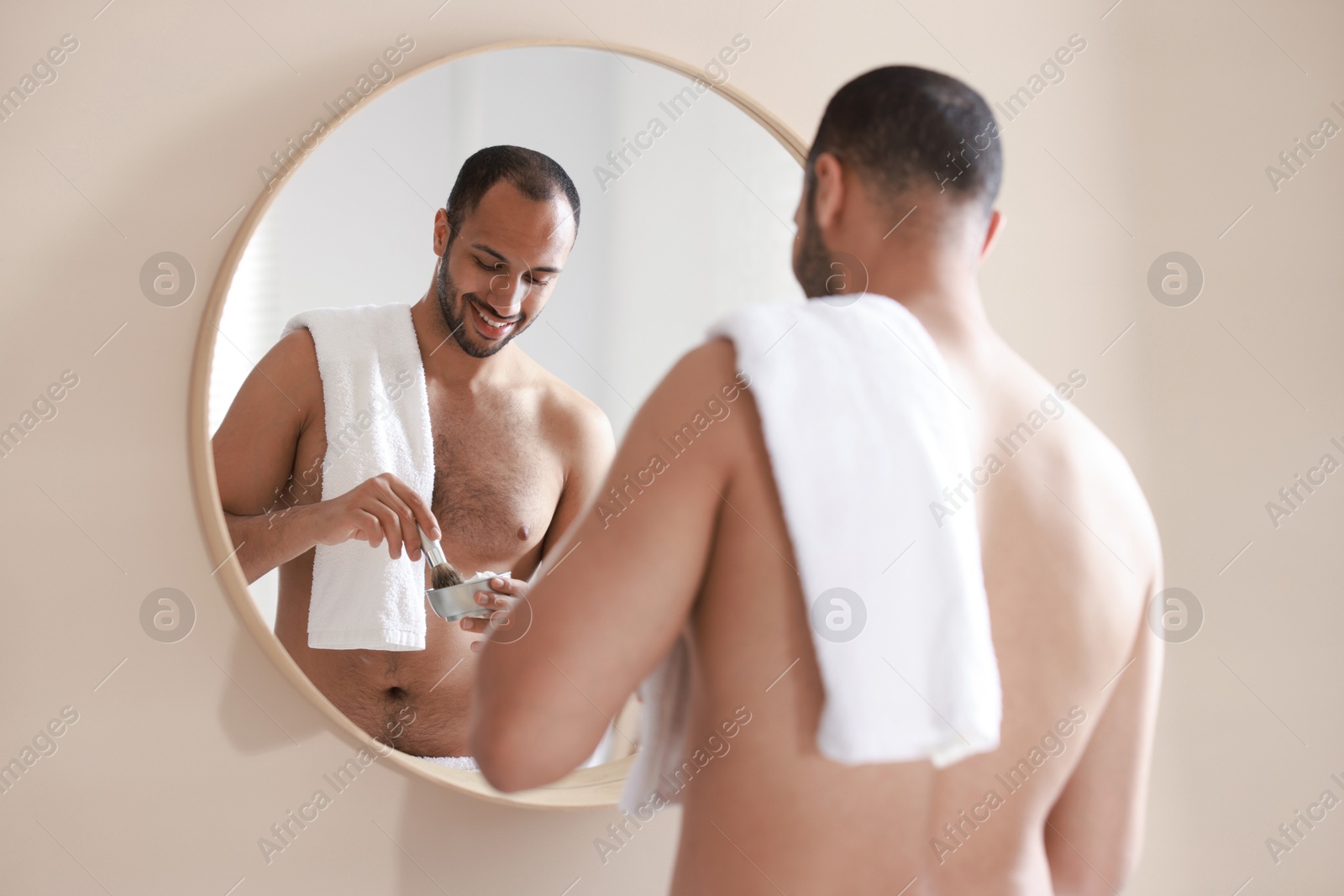 Photo of Smiling man with shaving foam near mirror in bathroom, back view