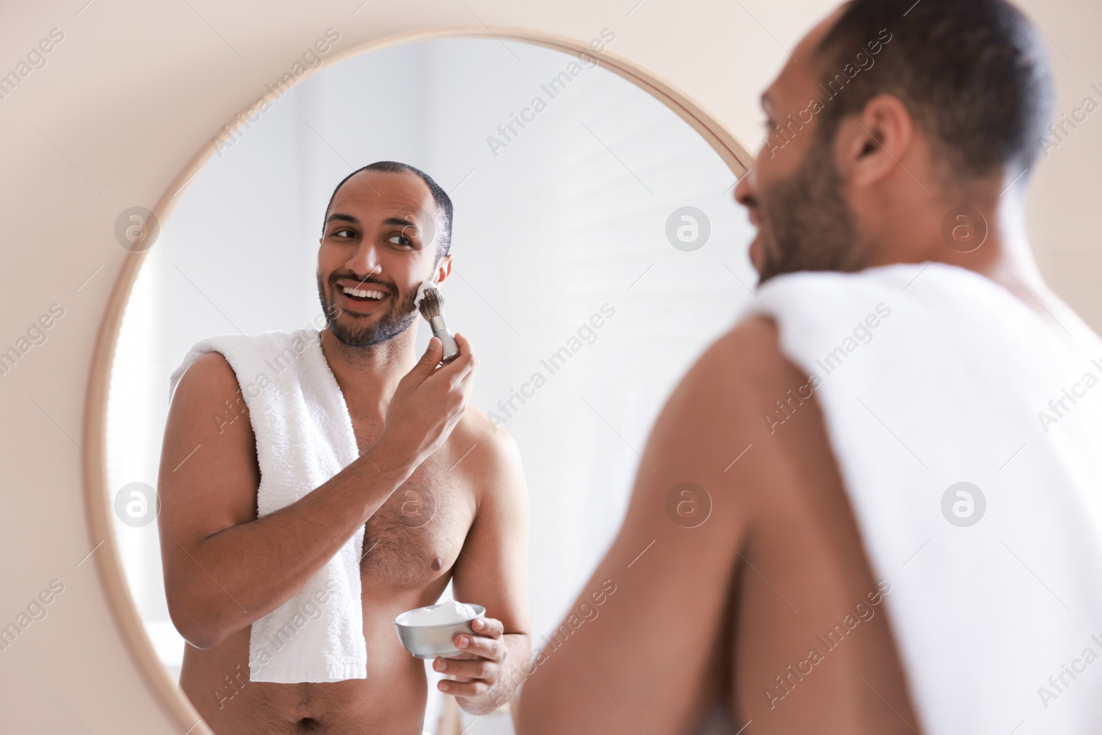 Photo of Smiling man applying shaving foam near mirror in bathroom