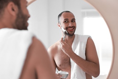 Photo of Smiling man applying shaving foam near mirror in bathroom