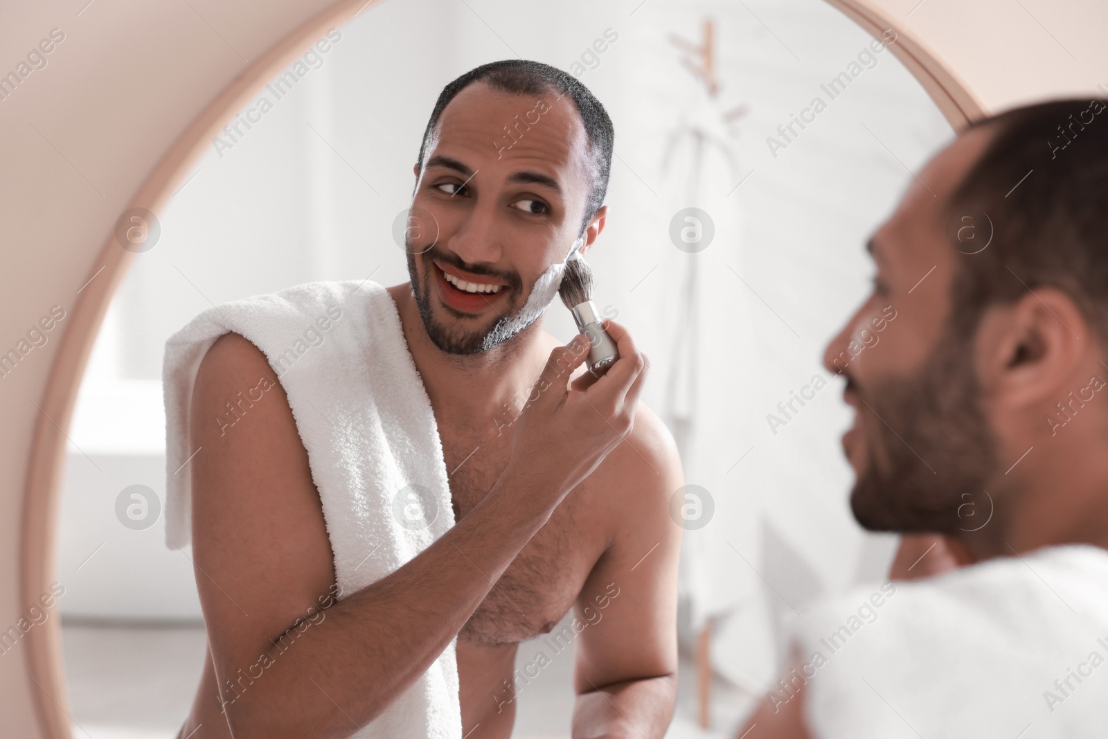 Photo of Smiling man applying shaving foam near mirror in bathroom