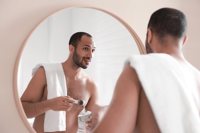 Photo of Smiling man with shaving foam near mirror in bathroom