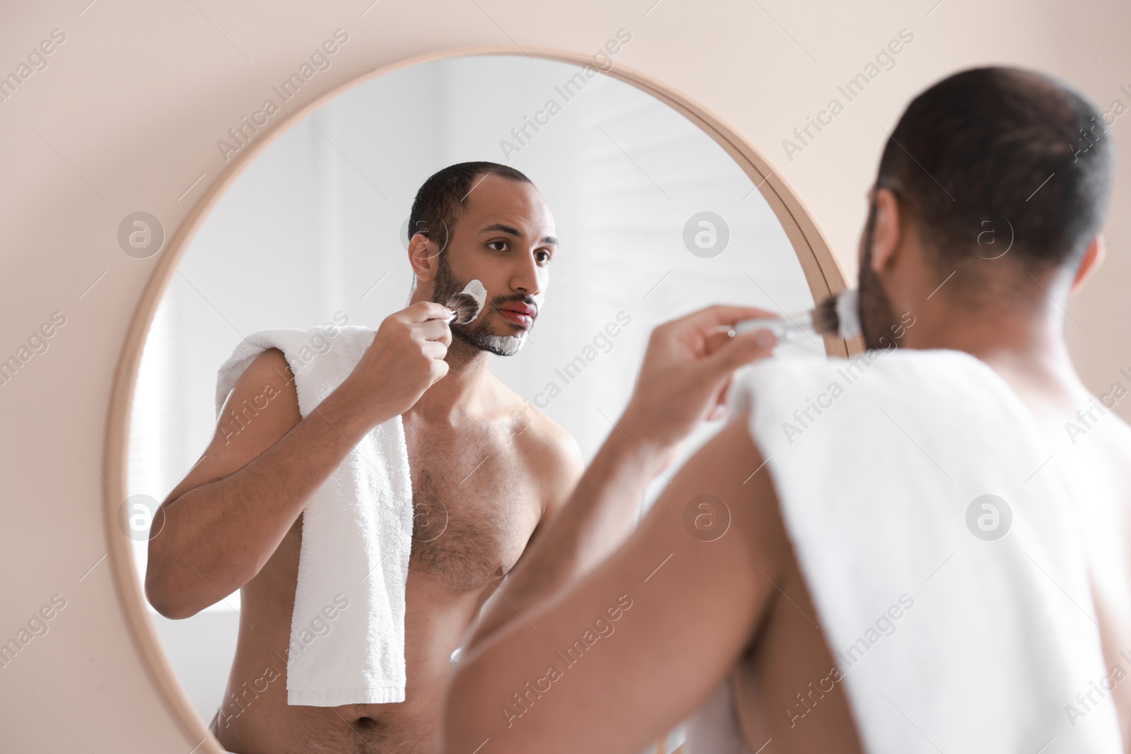 Photo of Handsome man applying shaving foam near mirror in bathroom