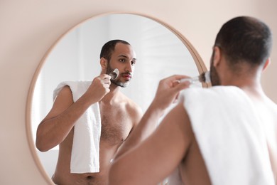 Photo of Handsome man applying shaving foam near mirror in bathroom