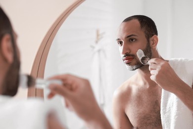 Handsome man applying shaving foam near mirror in bathroom