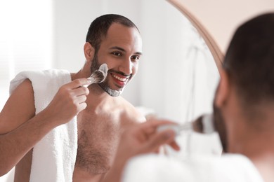 Photo of Smiling man applying shaving foam near mirror in bathroom