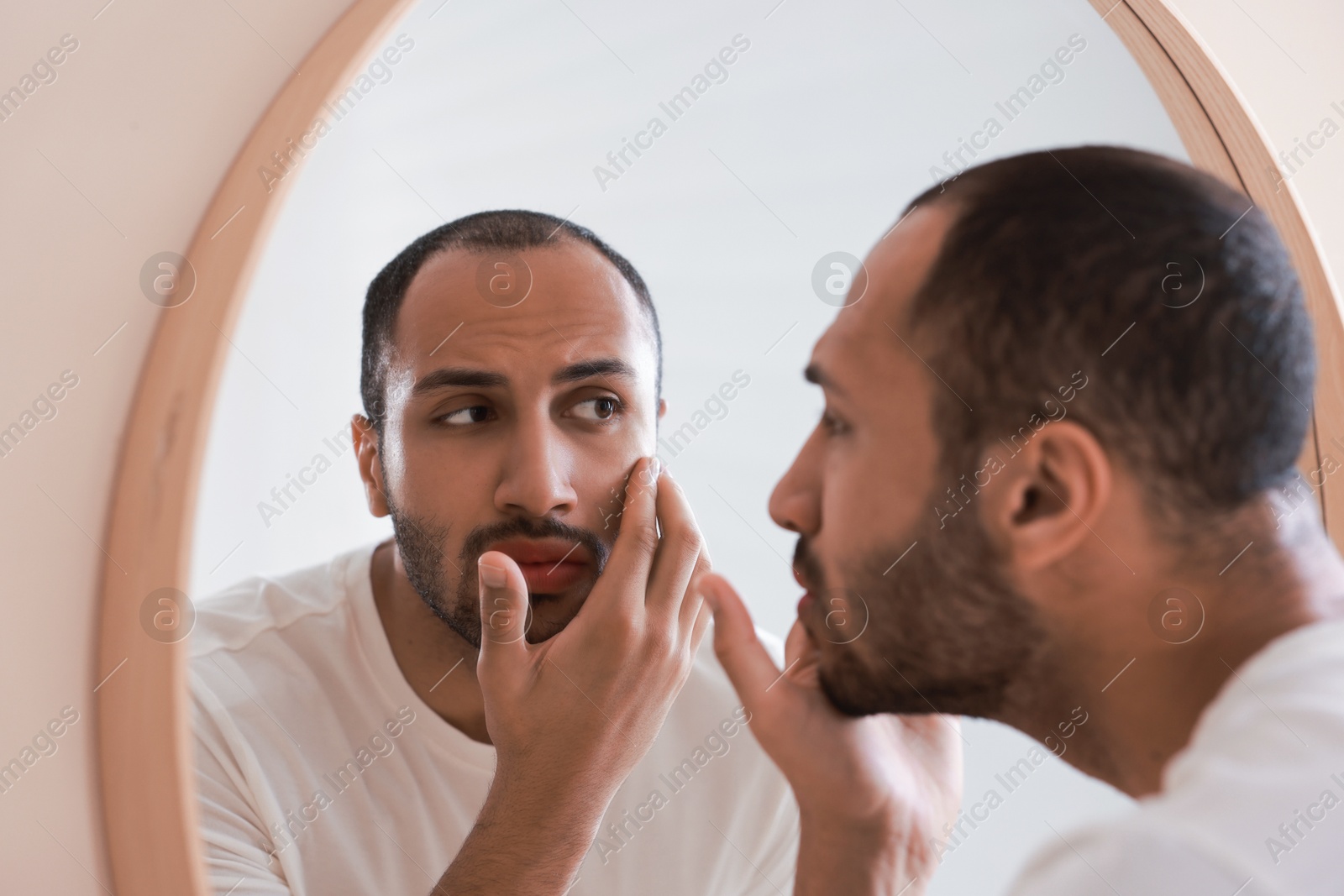 Photo of Worried man looking at mirror in bathroom