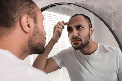 Photo of Worried man looking at mirror in bathroom